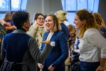 Three women standing in a crowded room, chatting excitedly